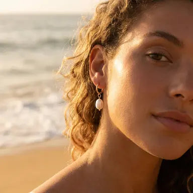 Woman wearing gold hoop with a pearl drop earrings with a beach background