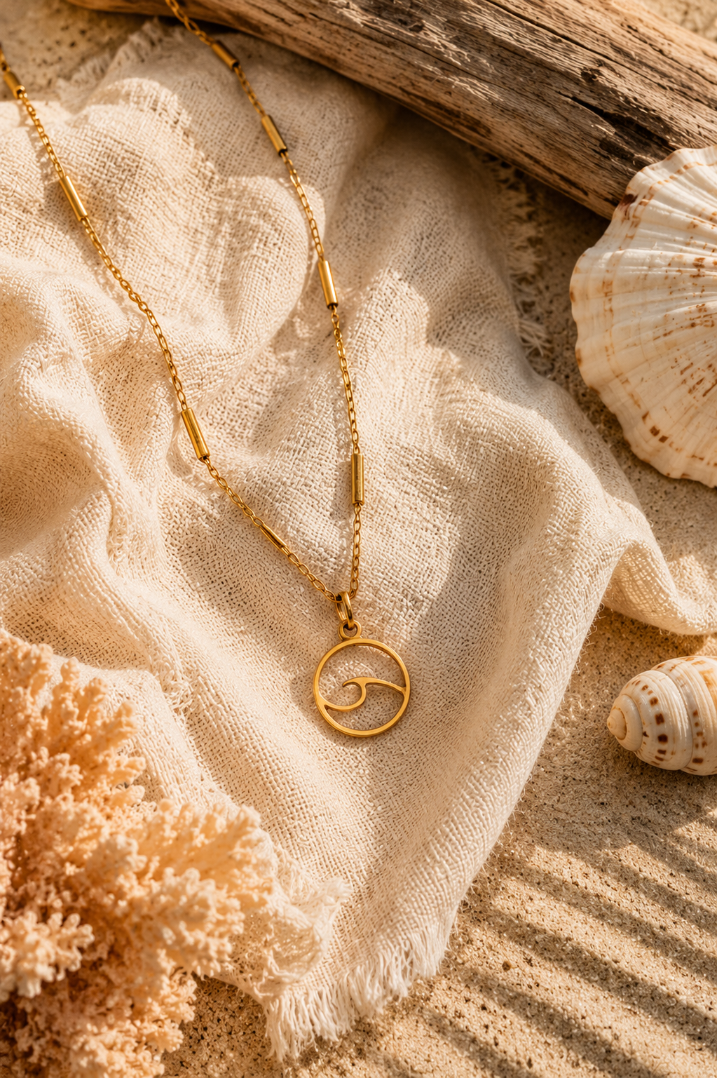 Gold necklace with a circular wave pendant on a textured beige surface with shells and coral.