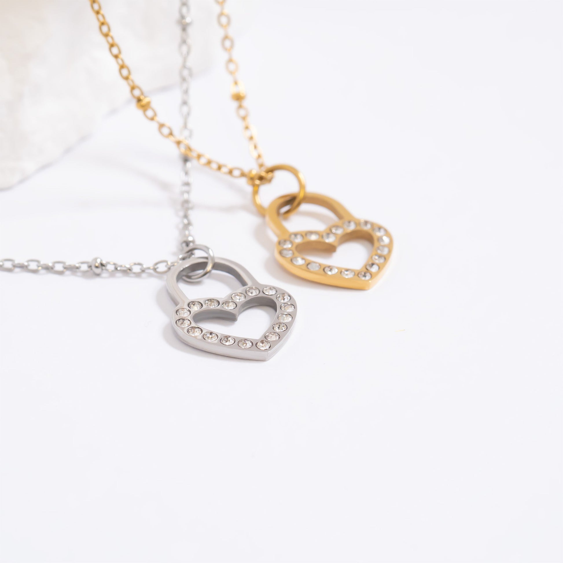 One silver and one gold chain with heart shaped padlock with diamonds embedded in each one on a white background