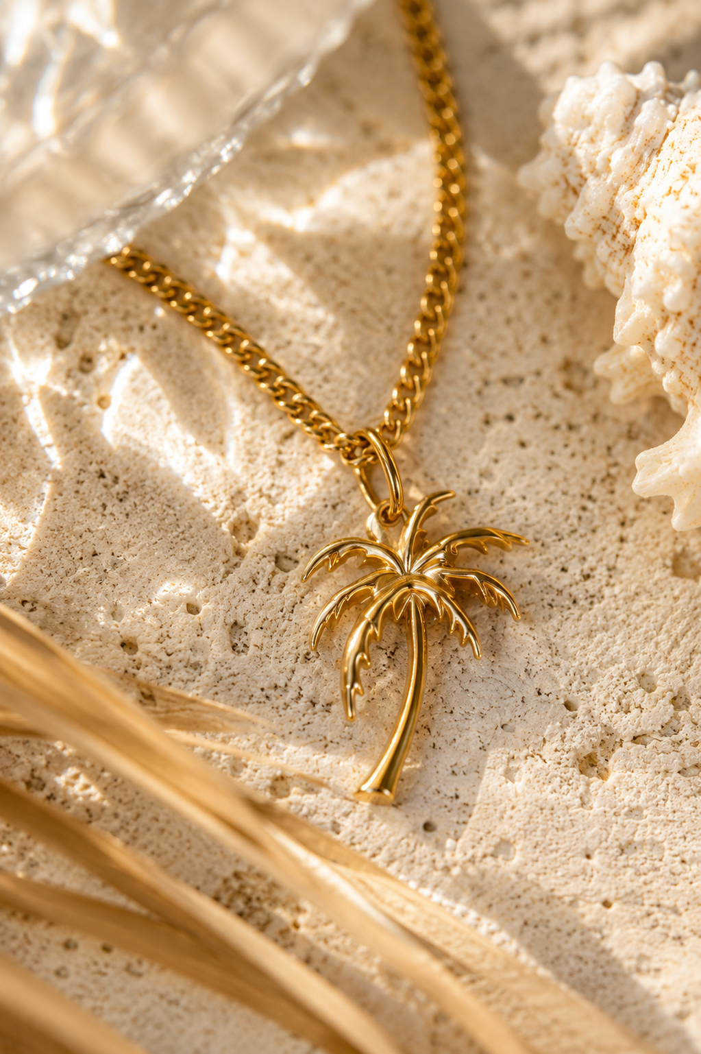 Gold chain with palm tree pendant lying on cream colored background.