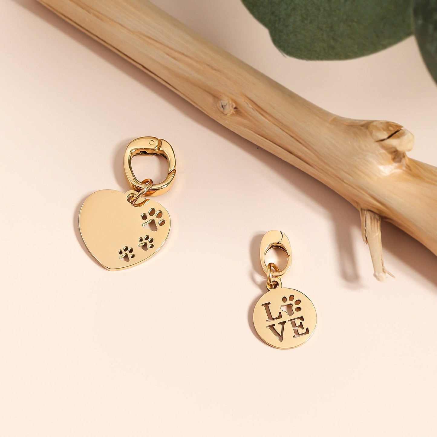 Gold heart-shaped charm with paw print and round 'LOVE' charm on a beige background