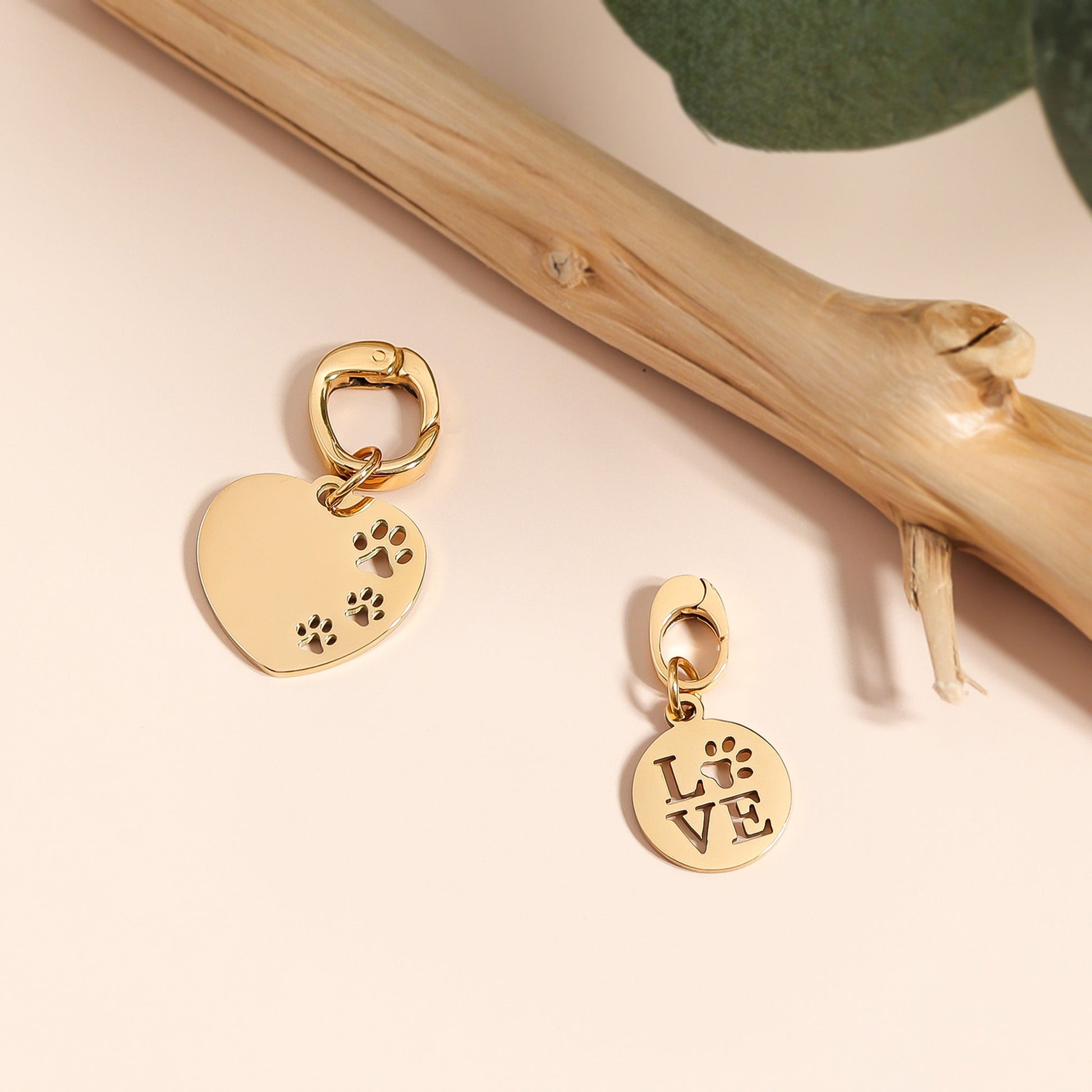 Gold heart-shaped charm with paw print and round 'LOVE' charm on a beige background