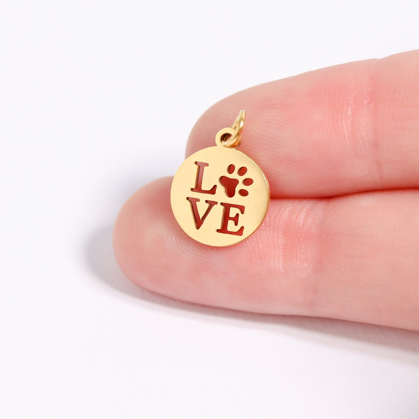 Gold pendant with 'LOVE' and paw print on a finger against a white background
