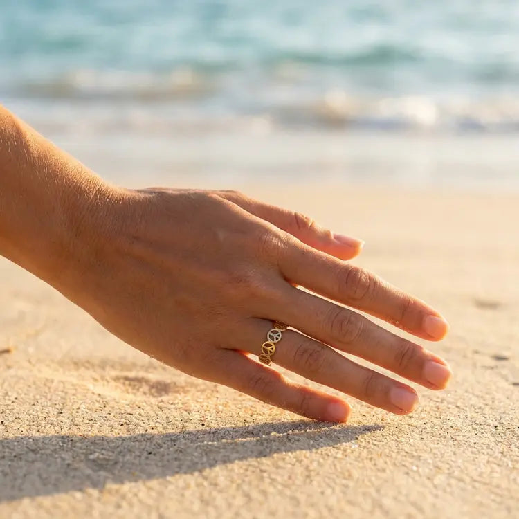 Hand with a peace sign ring on a sandy beach with ocean in the background