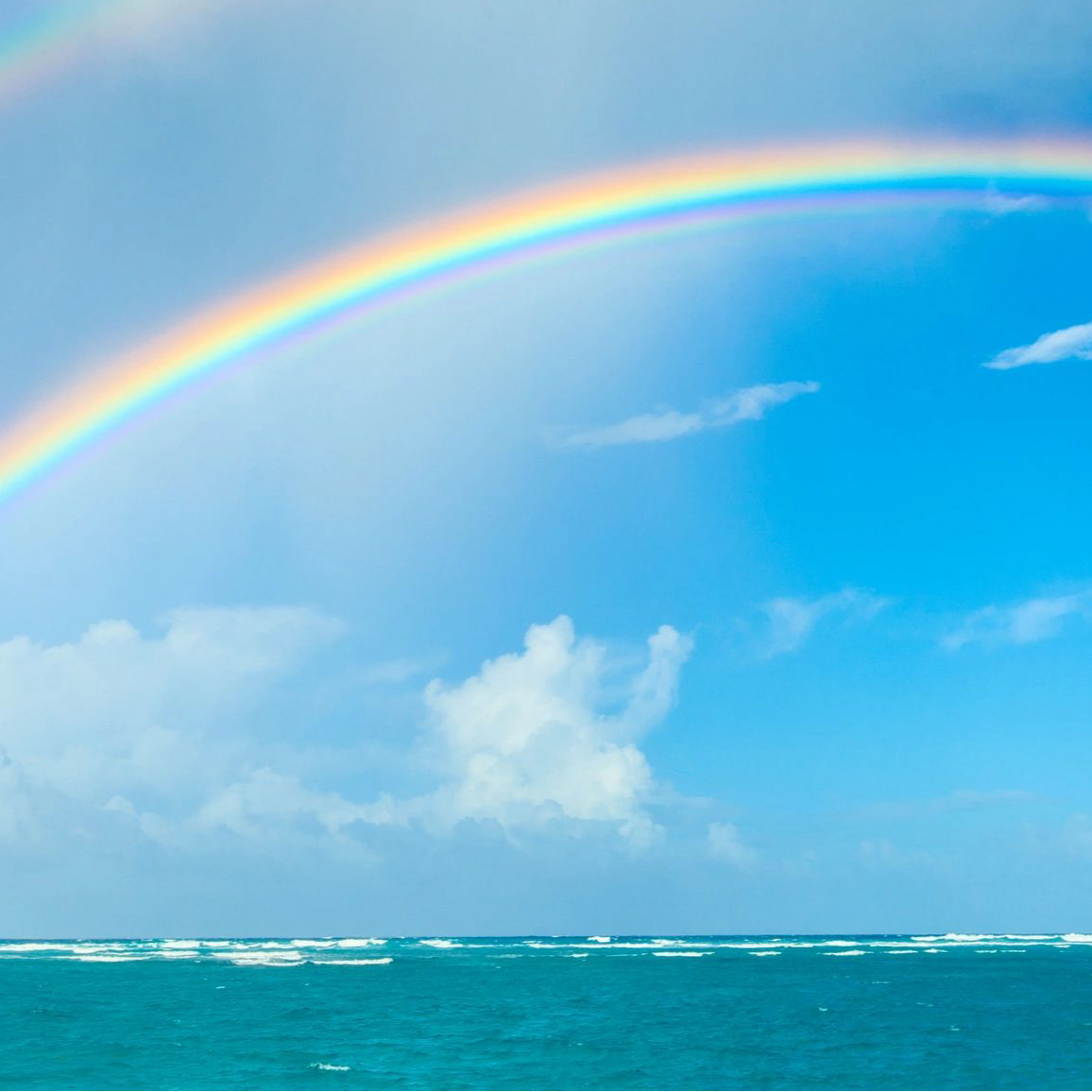 Double rainbow over a blue ocean with scattered clouds