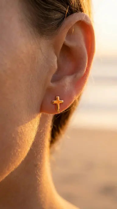Close-up of an ear wearing a gold cross earring with a blurred background