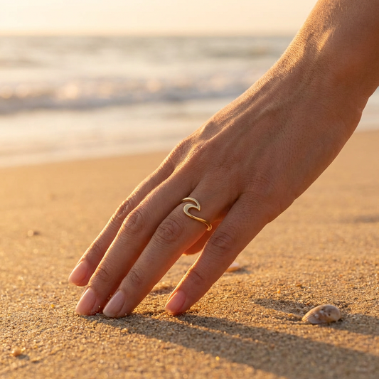 Hand with a gold ocean wave ring on a sandy beach at sunset