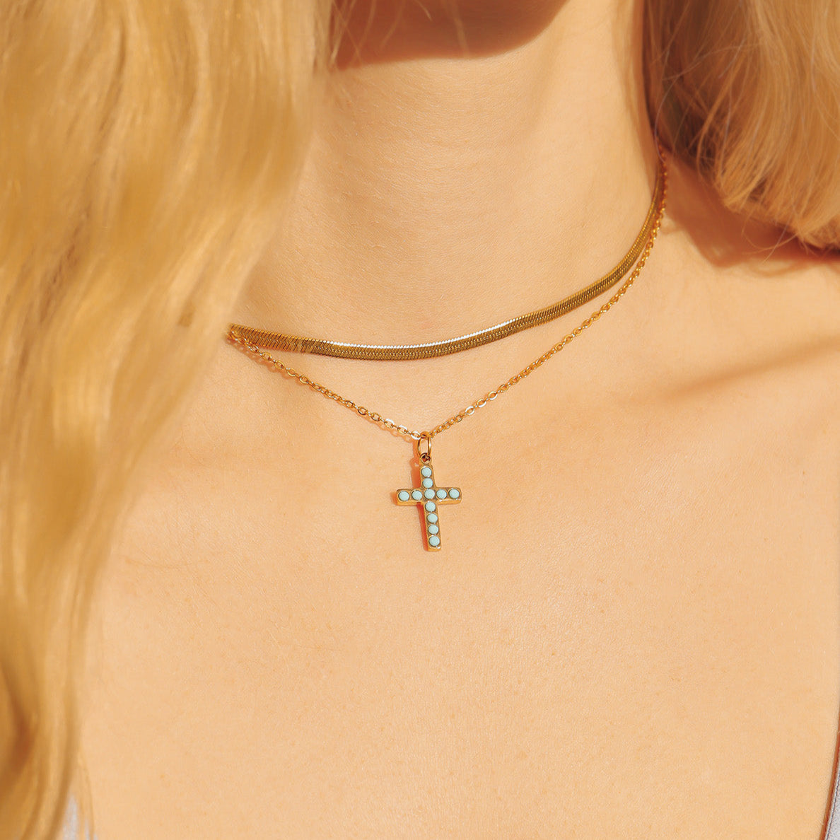 Gold necklace with a cross pendant worn by a person with blonde hair.
