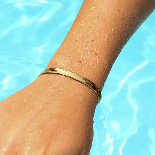 Gold herringbone bracelet on a wrist with a blue water background