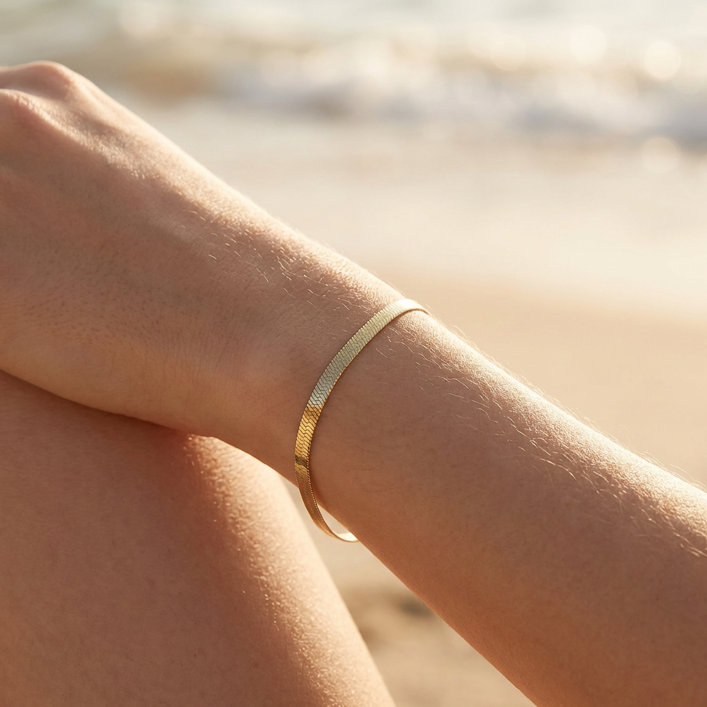 Gold herringbone bracelet on a wrist with a blurred natural background