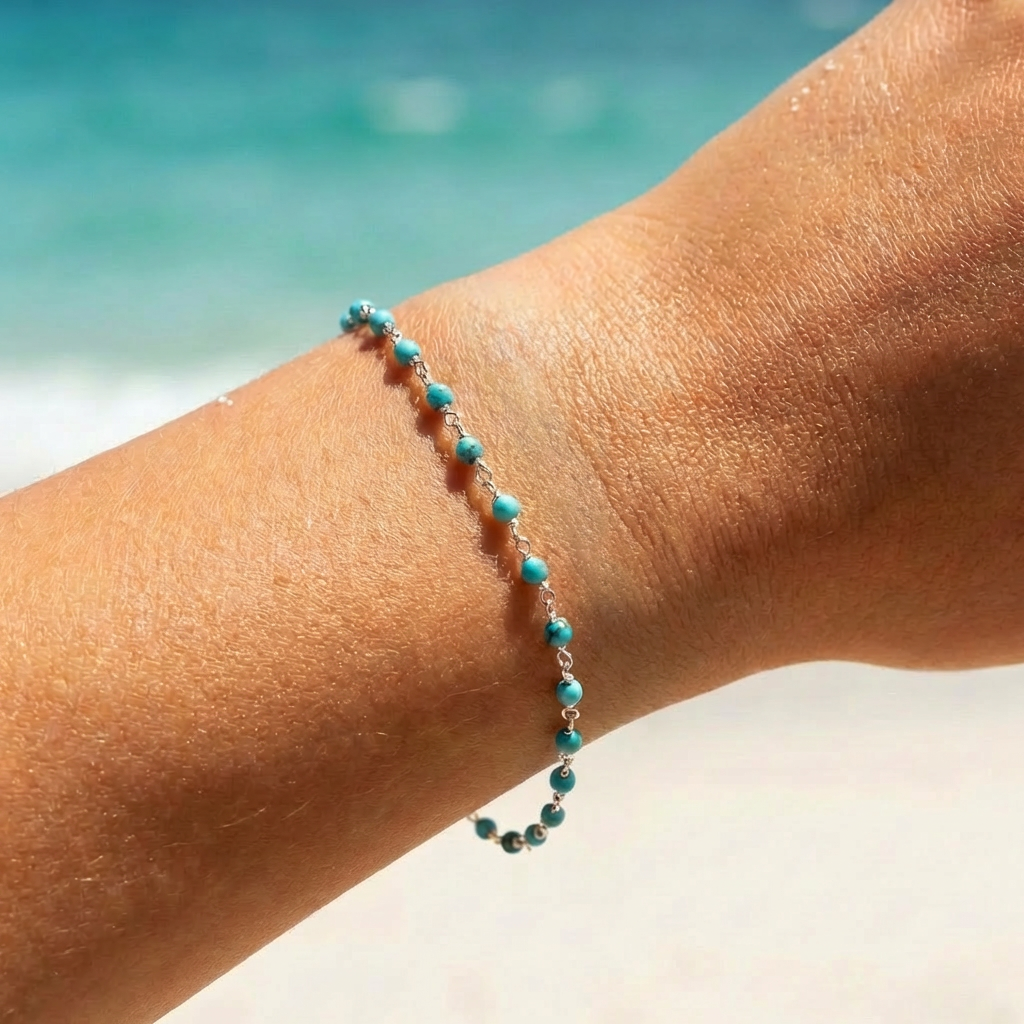 Silver bracelet with turquoise beads on a wrist with a beach background
