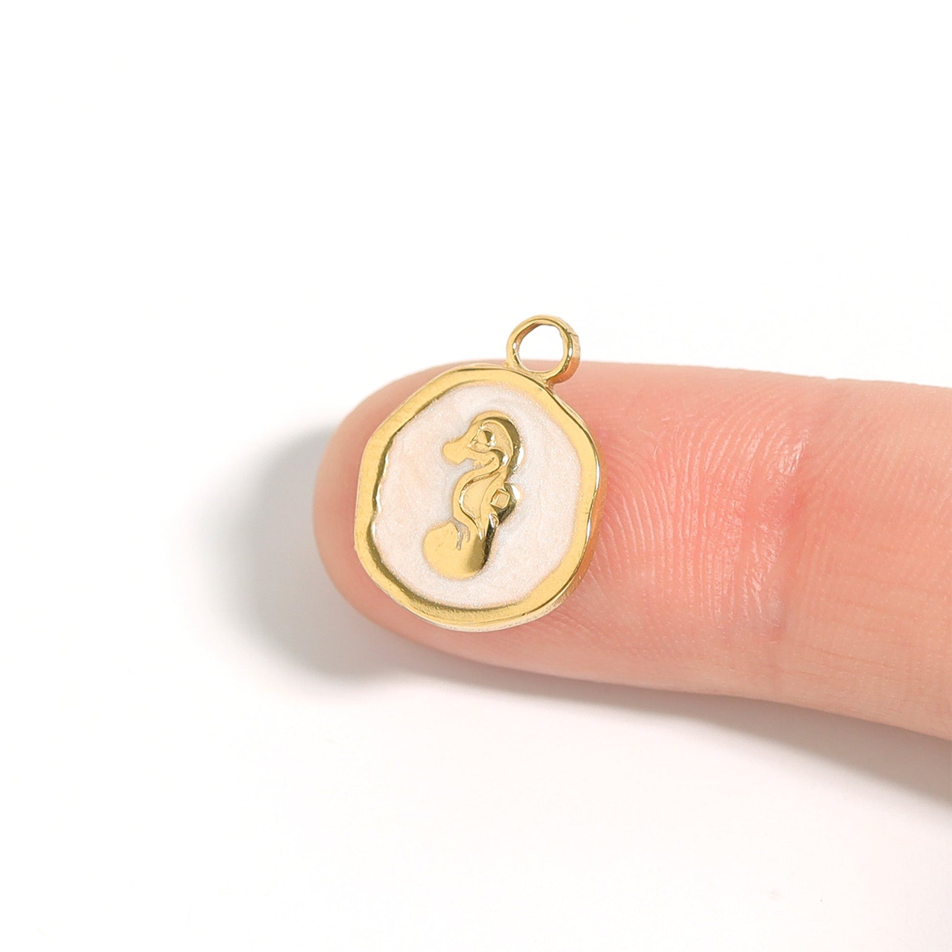 Circular gold pendant with seahorse in the center sitting on the tip of an index finger against a white background