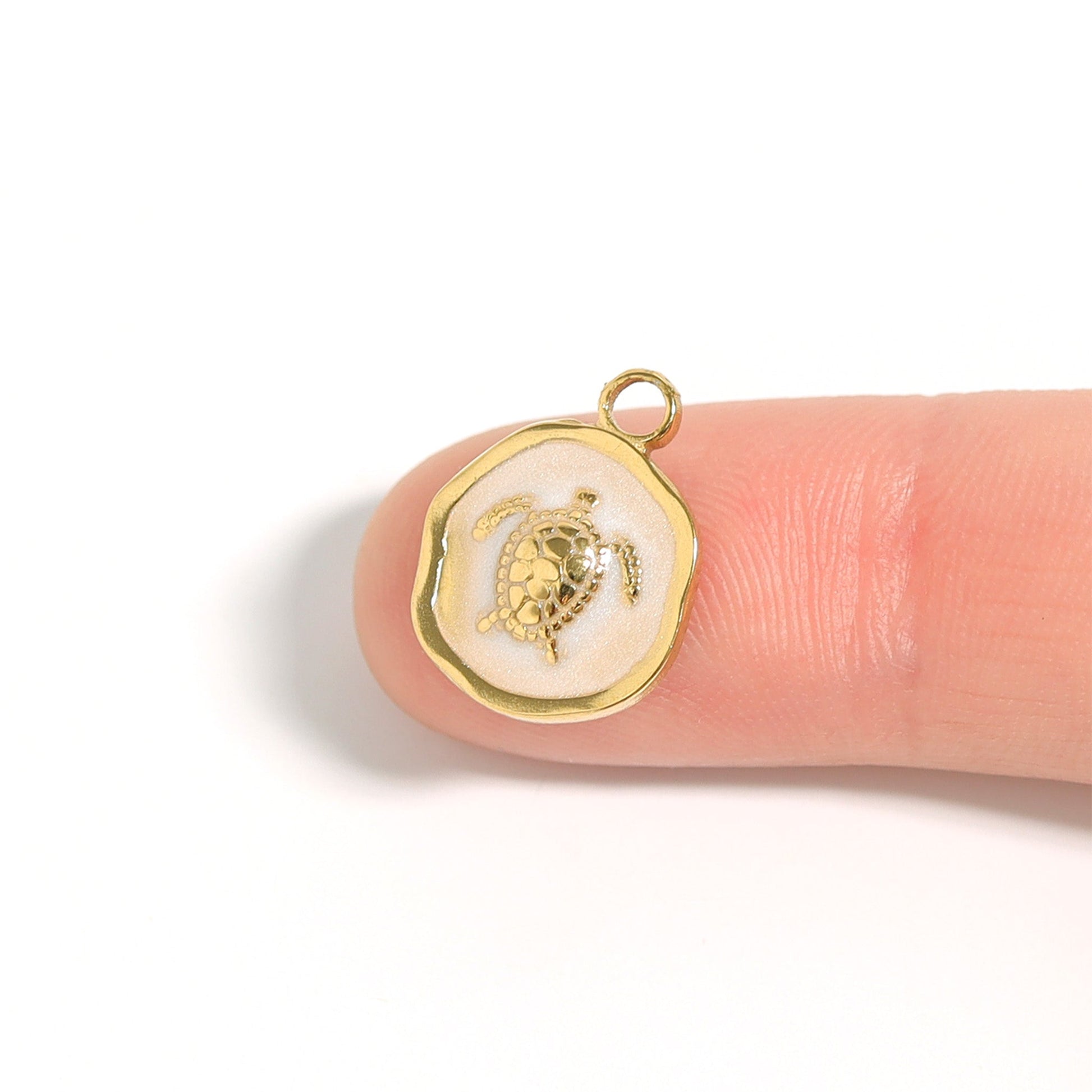 Gold circular pendant with a sea turtle in the center on the tip of a pointer finger against a white background