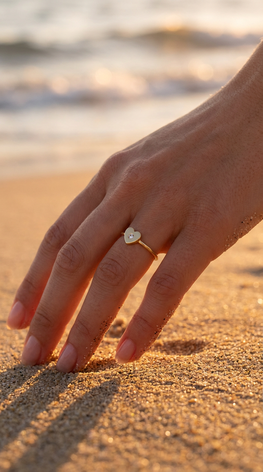Hand with a gold heart-shaped ring on a sandy beach at sunset