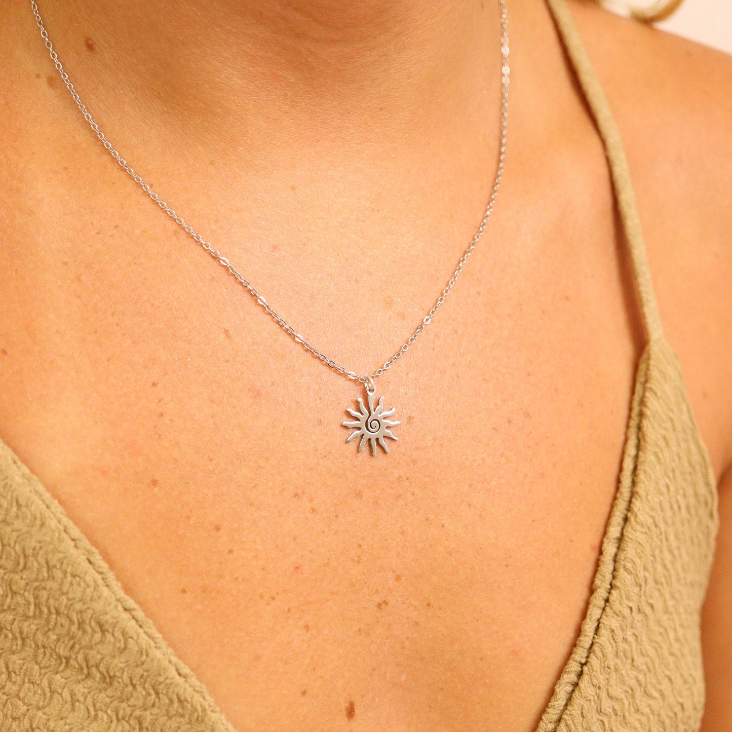 Silver sun-shaped necklace worn by a person in a green top against a neutral background