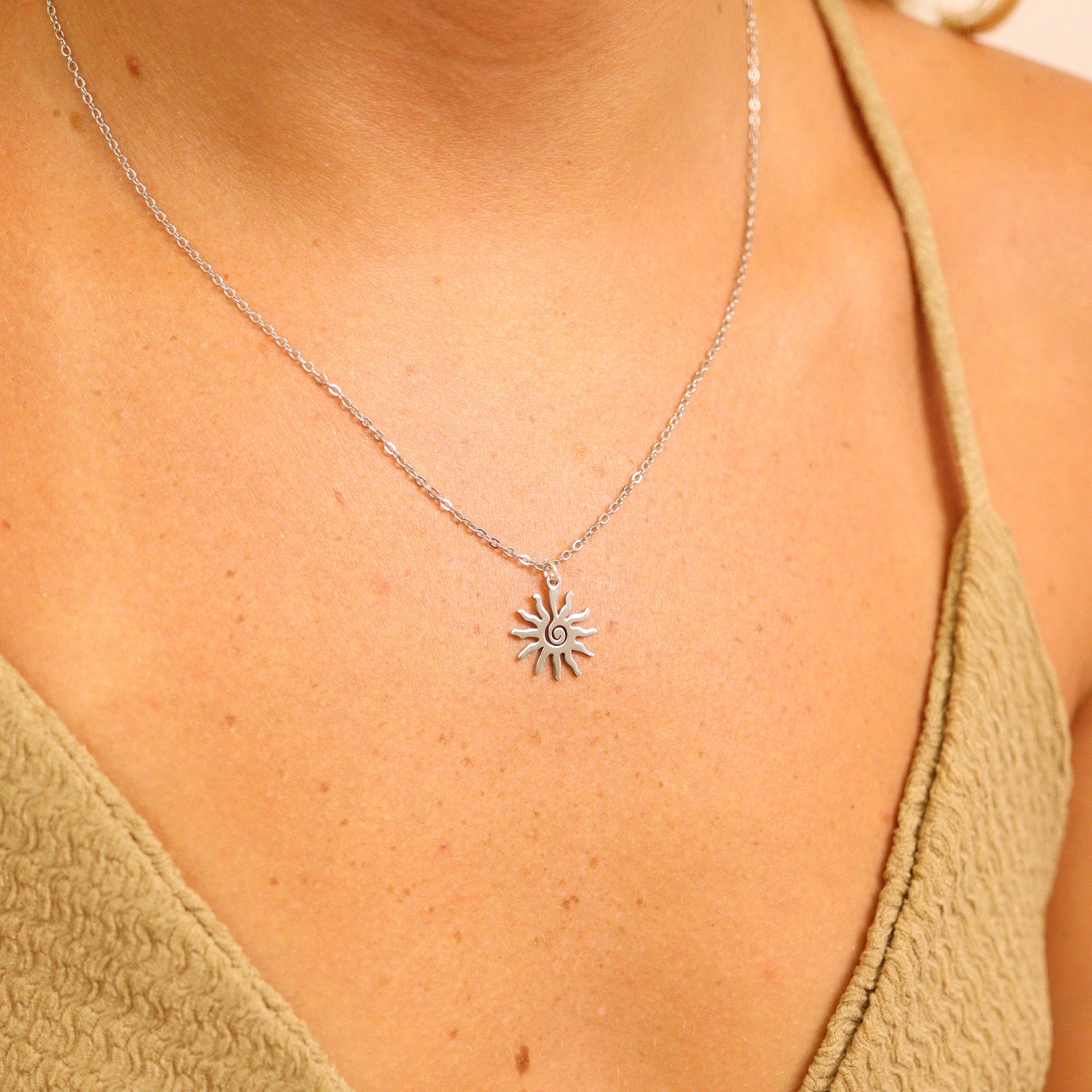 Silver sun-shaped necklace worn by a person in a green top against a neutral background