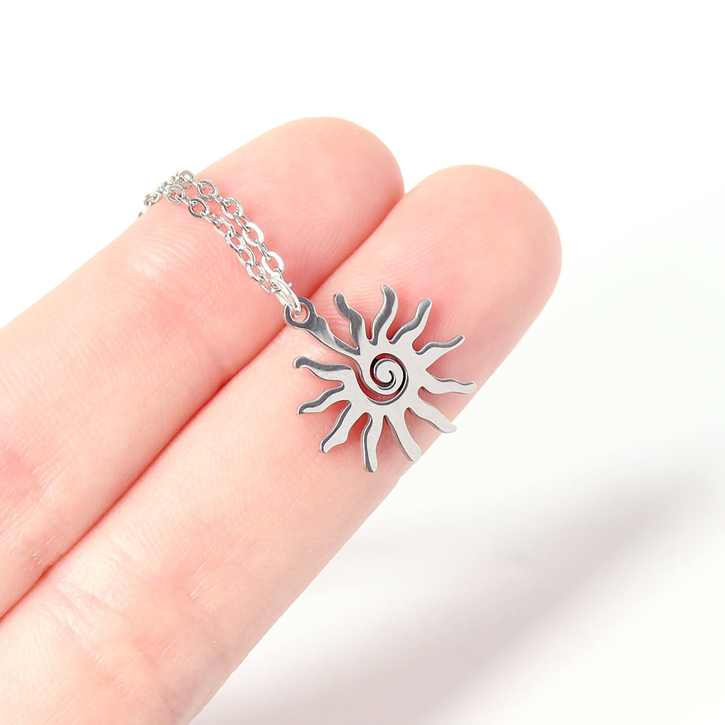 Silver sun-shaped pendant on a chain held between fingers against a white background
