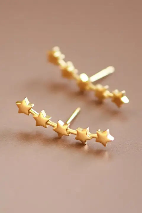 Gold star-shaped earrings on a beige background