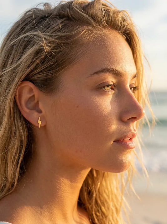 Close-up of a woman wearing a gold earring with a lightning bolt design, set against a blurred natural background.