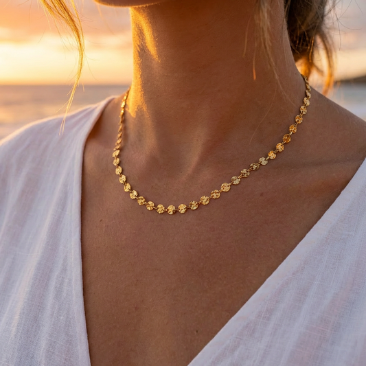Women in a white linen top wearing a gold necklace with mini suns at sunset on a beach