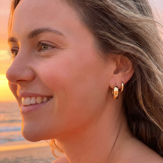 Woman wearing gold hoop earrings with a sunset beach background