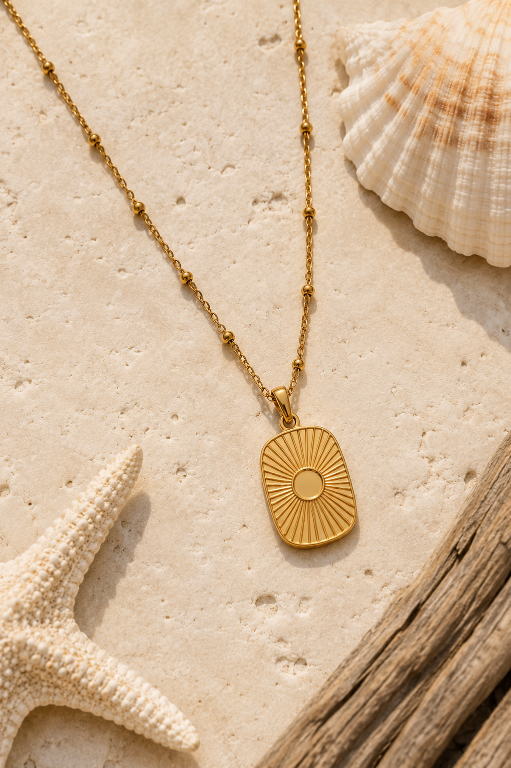 Gold satellite chain necklace with sunrays pendant lying next to shell, starfish, and driftwood.