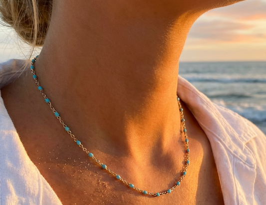 Necklace with turquoise beads worn by a person at sunset by the ocean