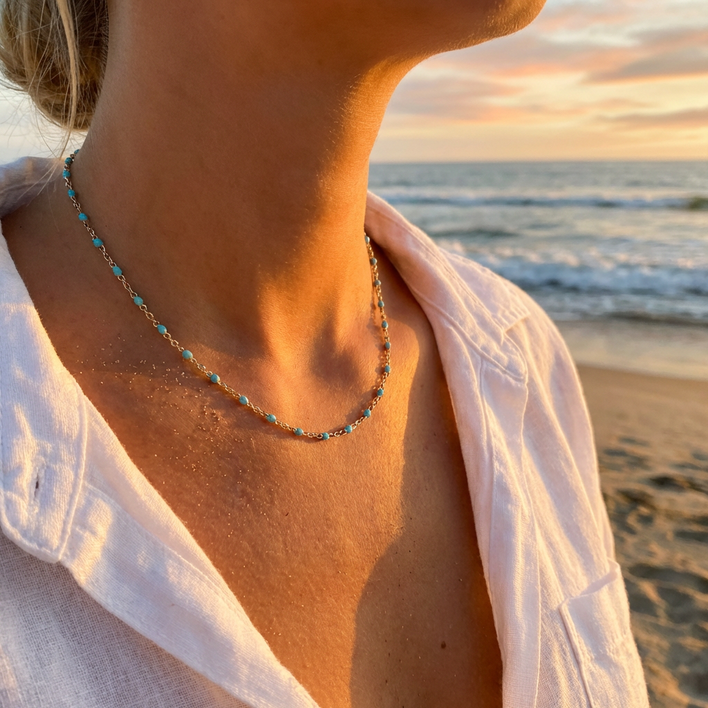 Person wearing a gold chain with turquoise beads with a beach and sunset in the background
