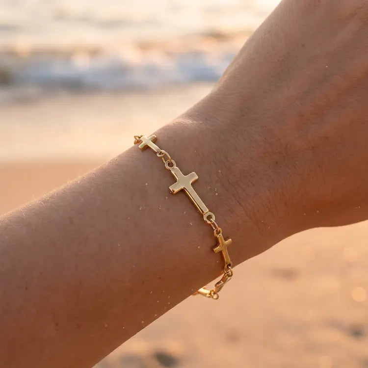 Gold bracelet with cross designs on a wrist against a beach background