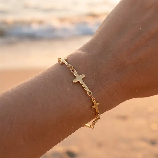Gold bracelet with cross designs on a wrist against a beach background