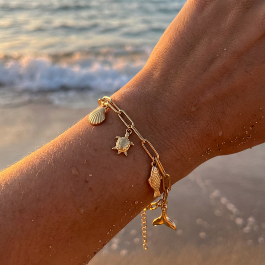 Gold bracelet with various sea creature charms on a wrist by the sea