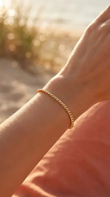 Close-up of a person's wrist wearing a gold rope bracelet with a blurred natural background