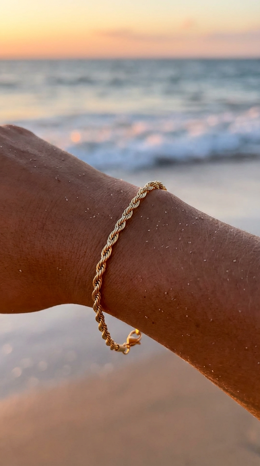 Gold rope bracelet on a wrist with a blurred beach and ocean background