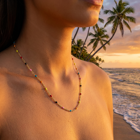Person wearing a colorful beaded and gold necklace on a beach with palm trees and sunset in the background