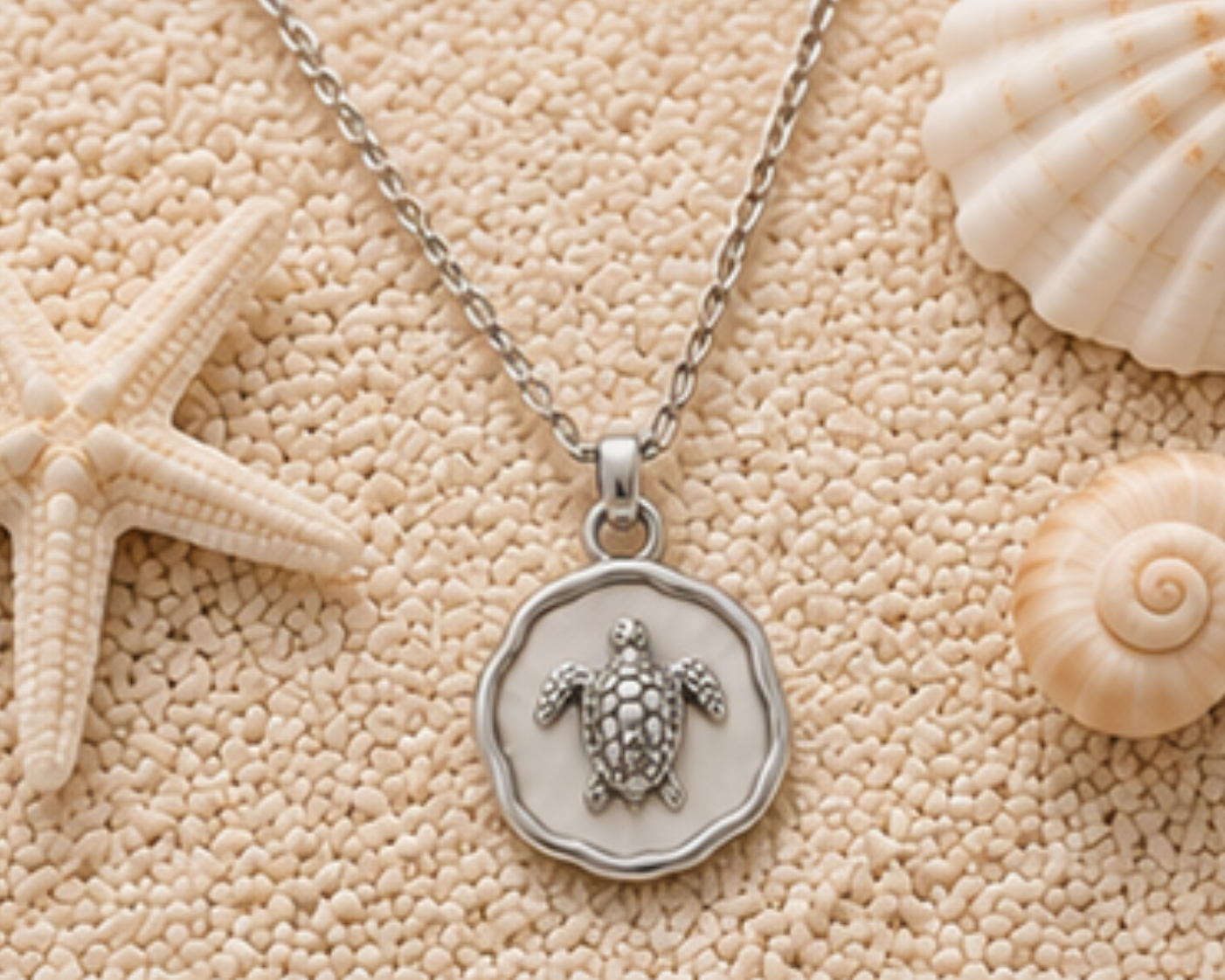 Silver chain with sea turtle pendant lying next to sea shells and a starfish.