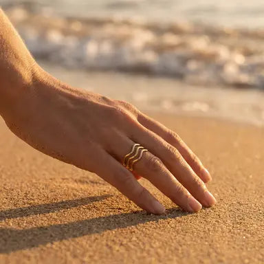 Hand with a gold wavy ring on a sandy beach 
