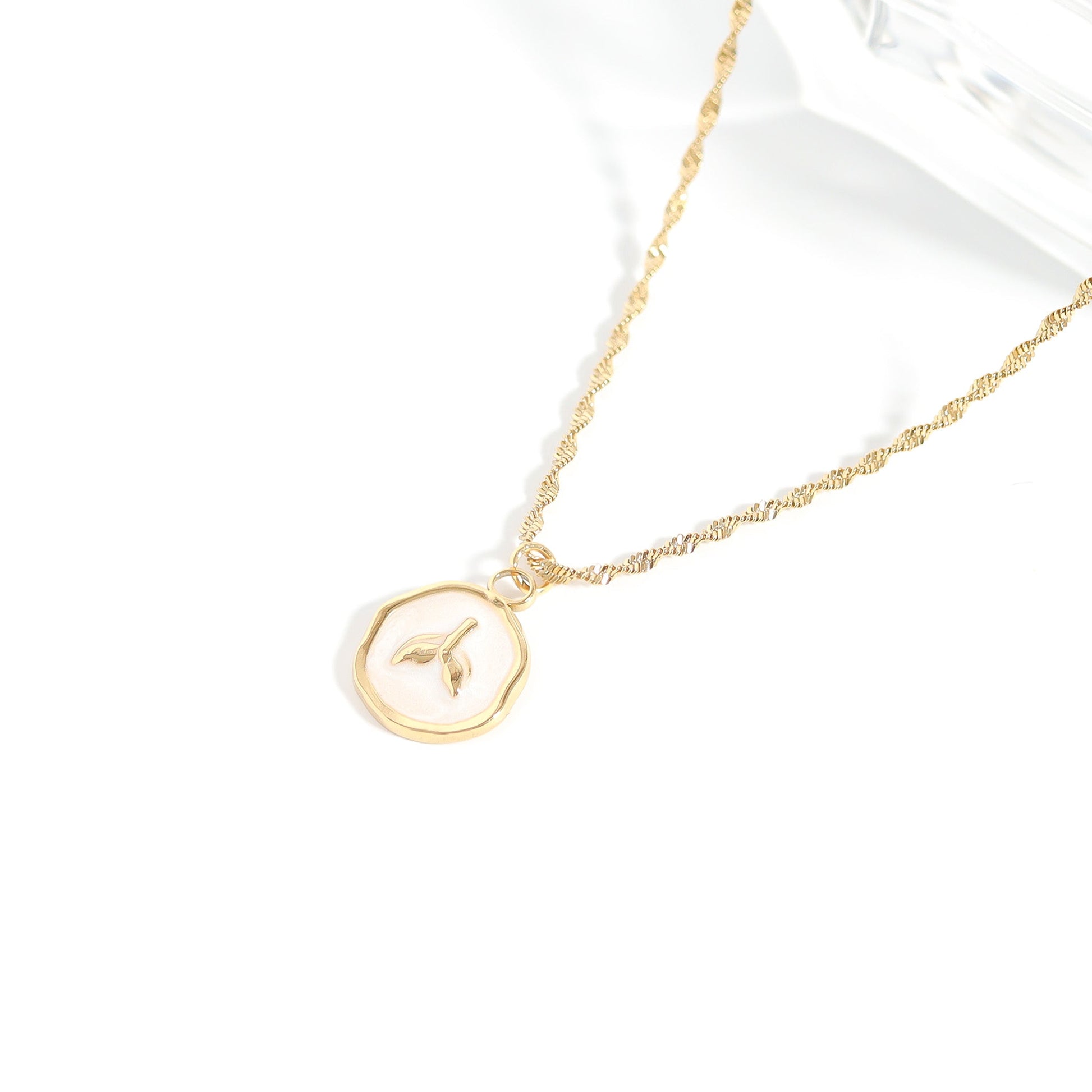 Gold chain with a circular pendant with a mermaid tail in the center on a white background