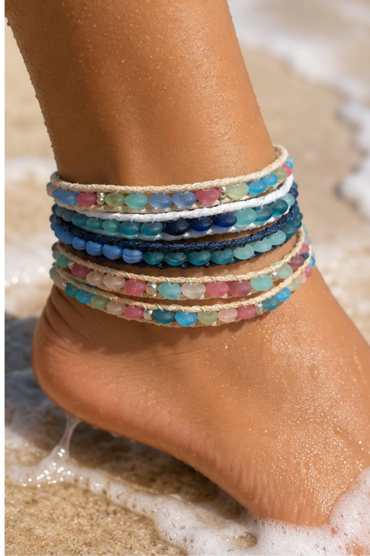 Colorful beaded anklets on a person's ankle with a beach background.