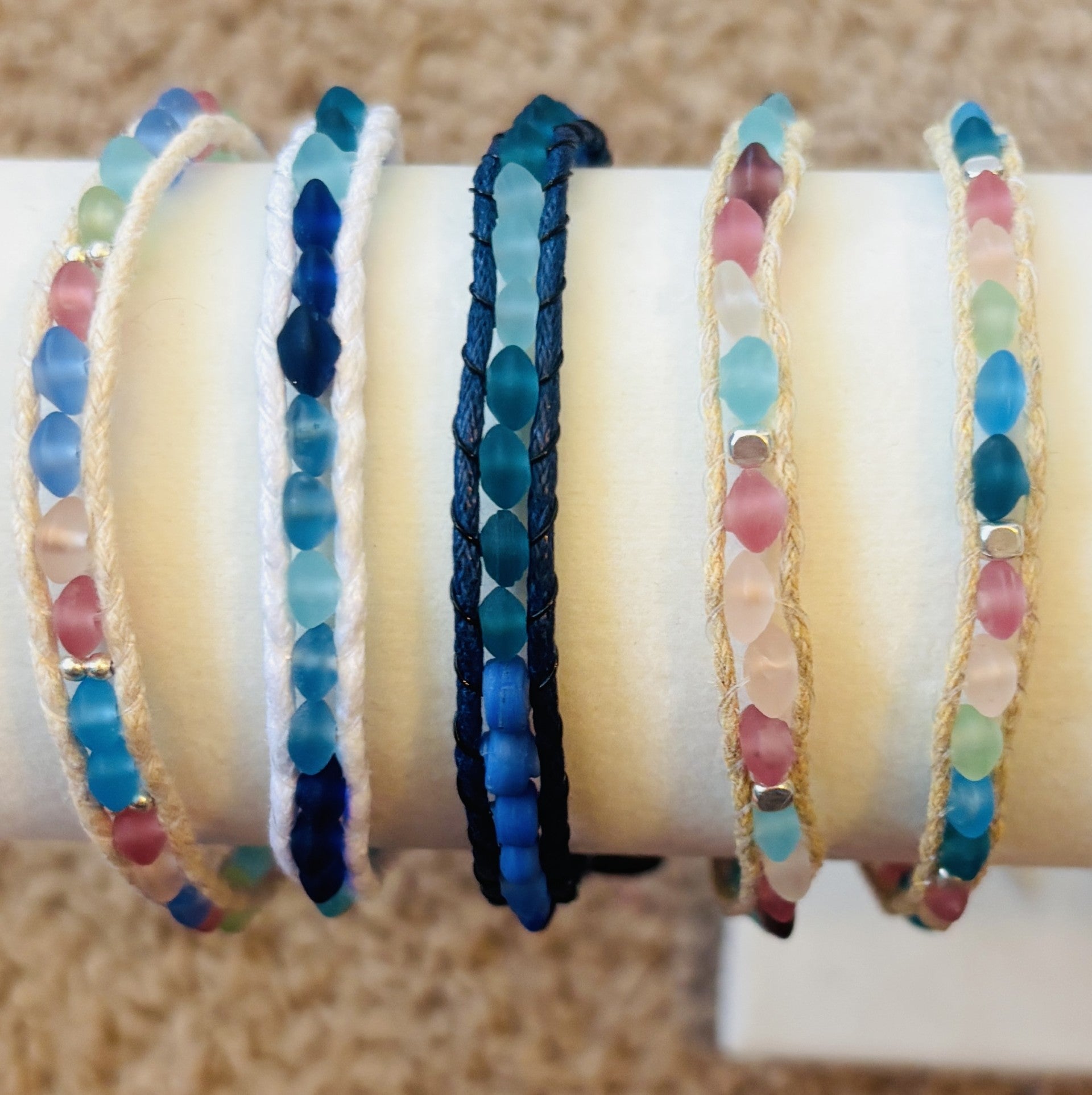 Set of colorful beaded bracelets on a white cylindrical stand.