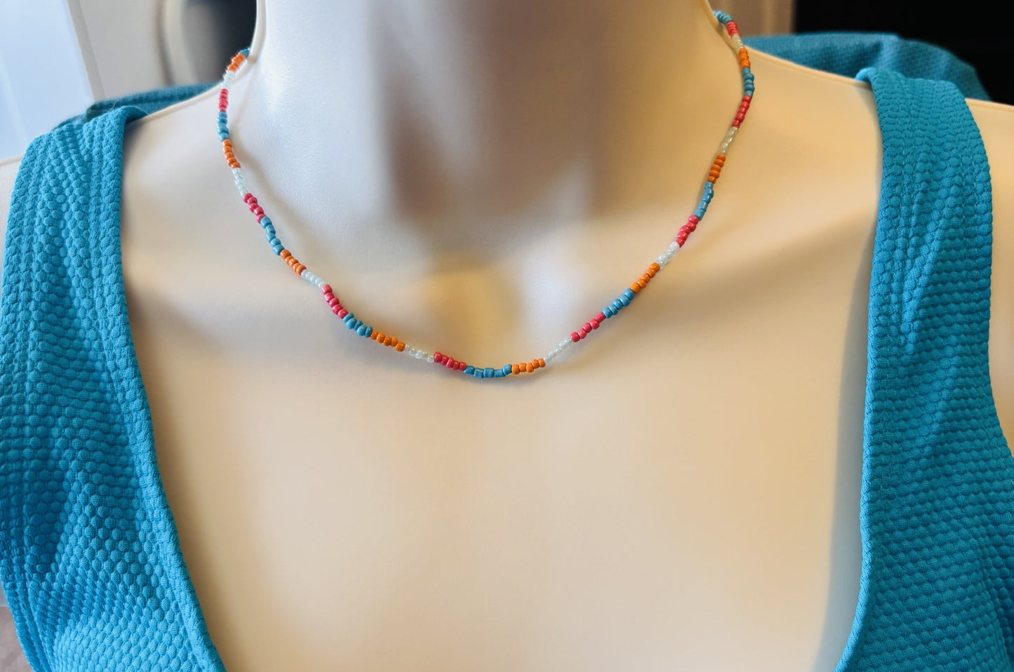 Mannequin wearing a colorful beaded necklace with a blue top.