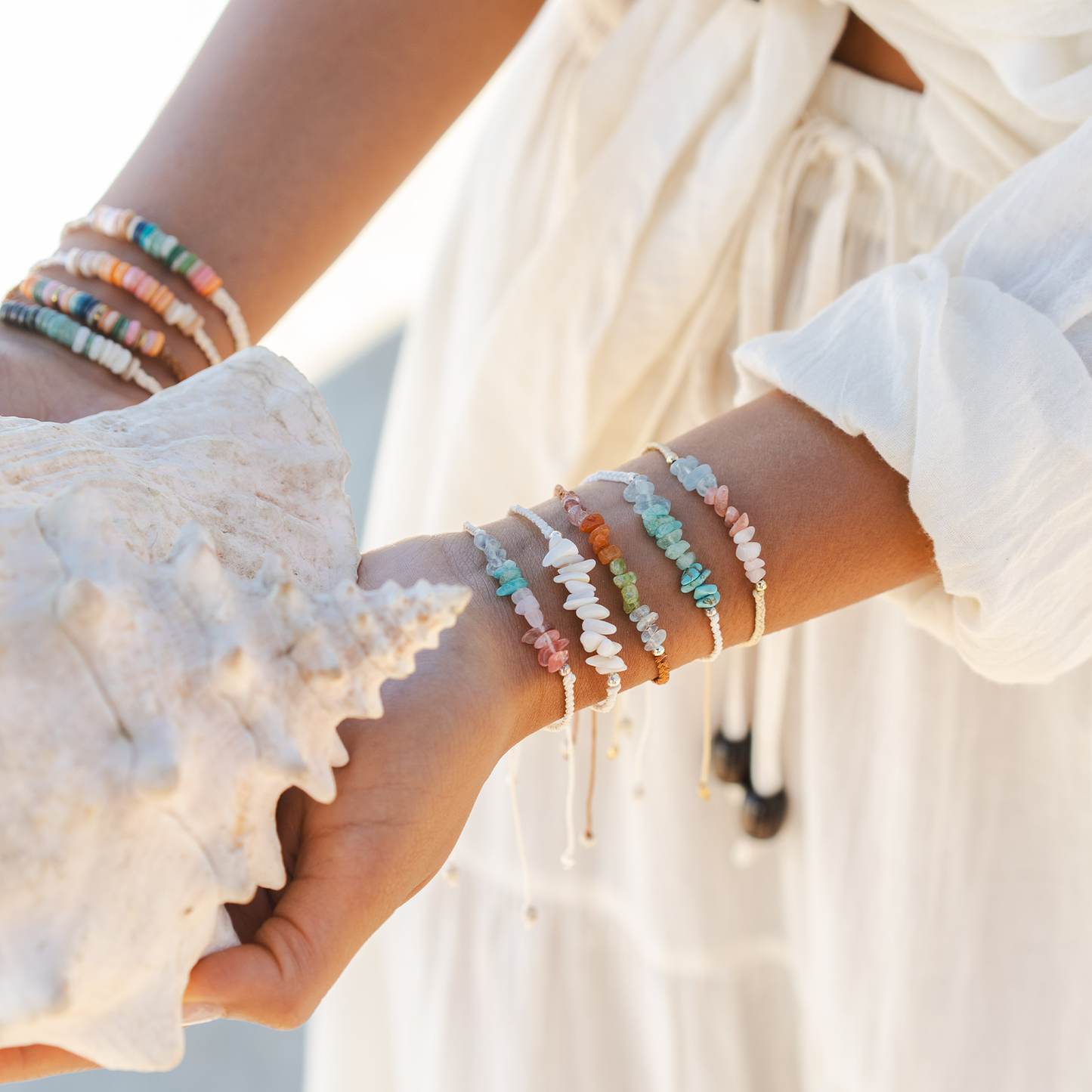 Close-up of a person's wrist wearing multiple colorful beaded bracelets with a shell in the background.