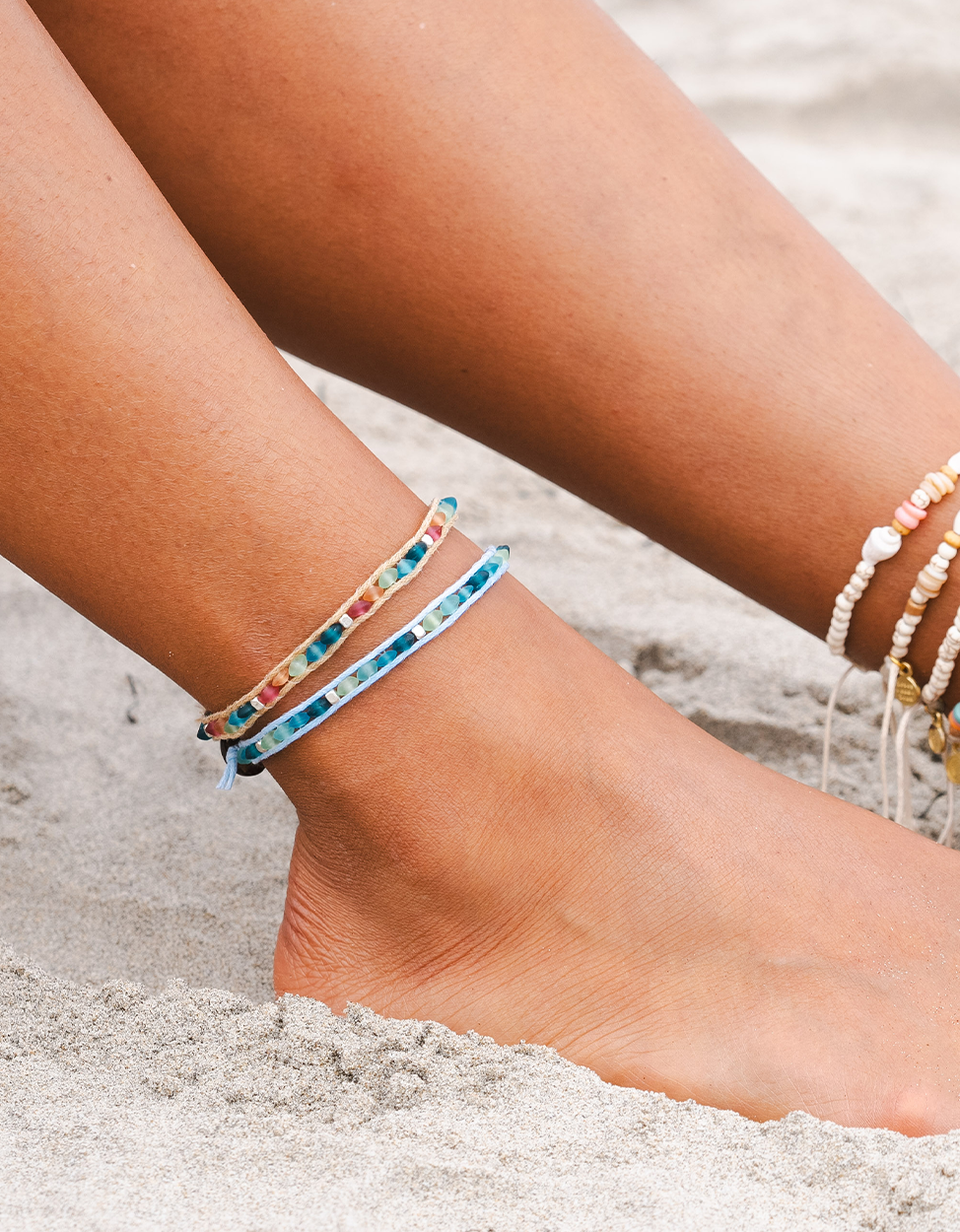 Close-up of feet with anklets on a sandy beach