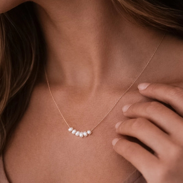 Pearl necklace on a person's neck with a hand touching the skin