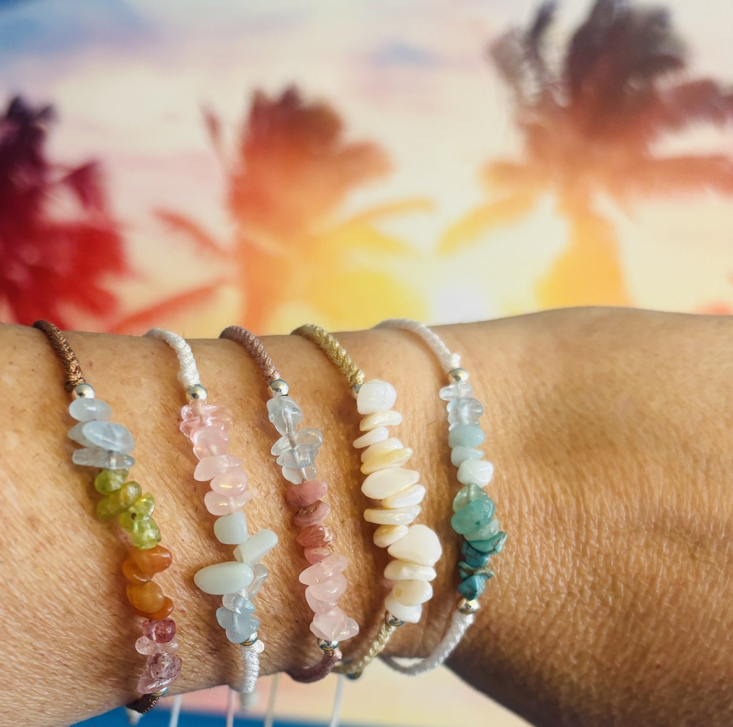 Close-up of a wrist wearing multiple colorful stone bracelets with a blurred natural background.