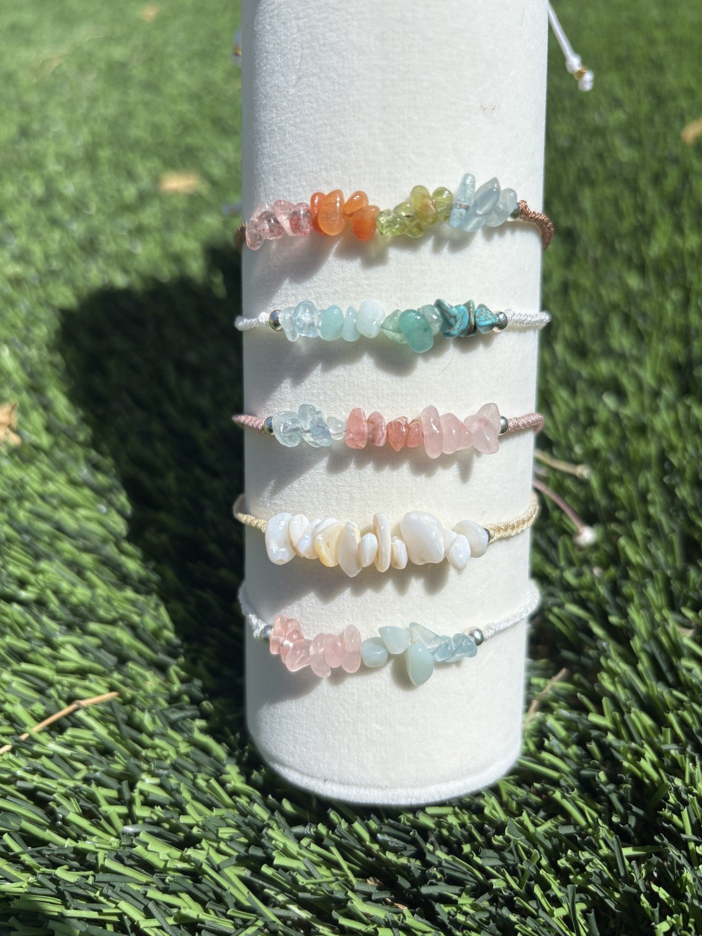 Set of colorful beaded bracelets on a white cylindrical stand against a grassy background