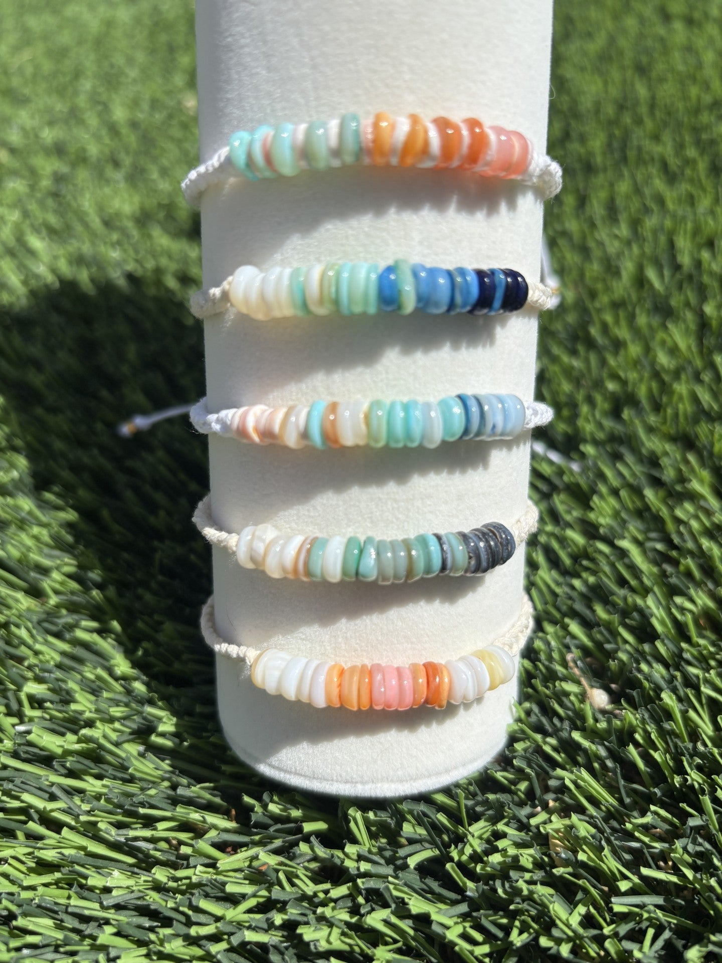 Set of colorful beaded bracelets on a white cylindrical holder against a grass background